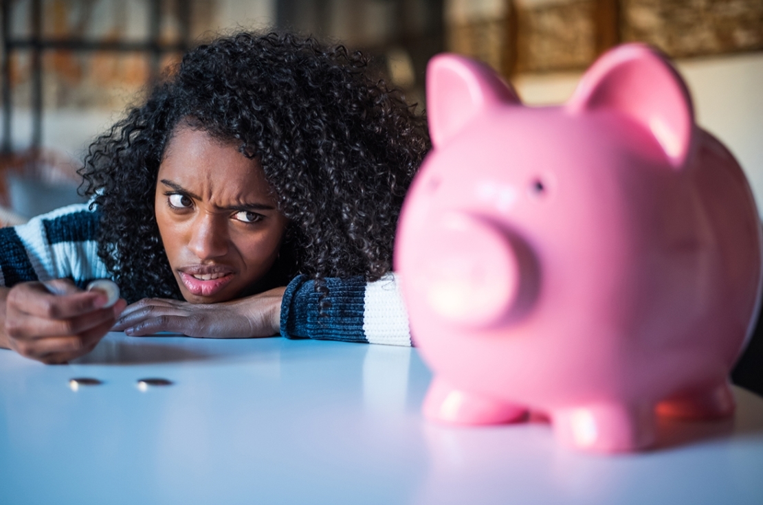 Confused woman looking at piggybank